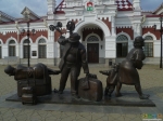 Скульптуры пассажиров на фоне старого вокзала.